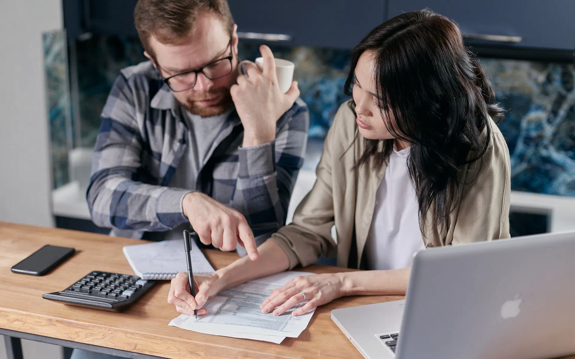 Casal sentado à mesa fazendo as contas juntos, com papéis, calculadora e notebook